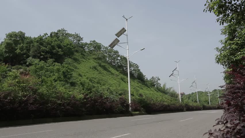 Two lane road with street lights beside lush green hillside on overcast day in rural China