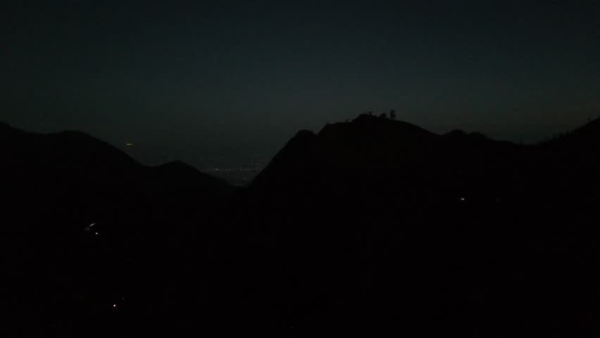 Mountain silhouettes at twilight with distant city lights and vehicle trails in the valley, creating a serene and vast landscape scene at dusk or dawn.