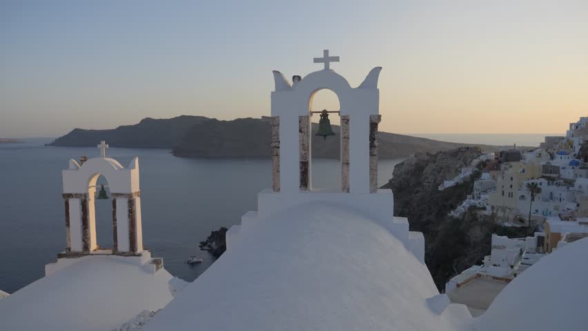 Pan across church bells and blue domes at sunset in Oía, Santorini, Greece.