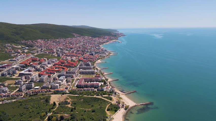 Beautiful panoramic aerial view of Sveti Vlas resort city with red roof hotels, turquoise Black Sea coastline and green Balkan mountains in Bulgaria.