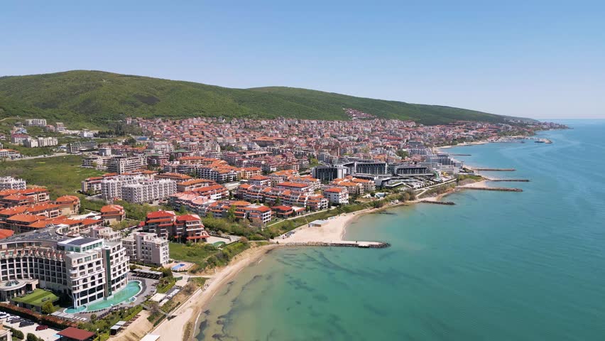 Beautiful panoramic aerial view of Sveti Vlas resort city with red roof hotels, turquoise Black Sea coastline and green Balkan mountains in Bulgaria.