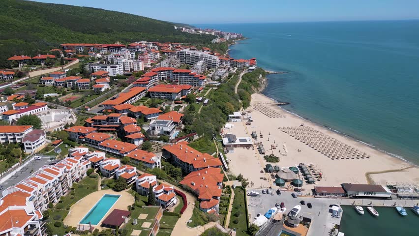 Beautiful panoramic aerial view of Sveti Vlas resort city with red roof hotels, turquoise Black Sea coastline and green Balkan mountains in Bulgaria.