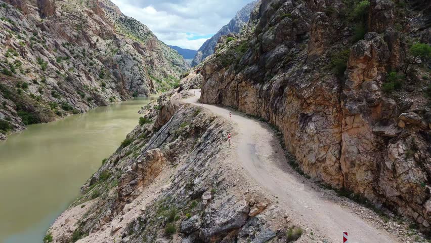 Aerial tracking shot over the dangerous historic stone road carved into steep cliffs of Karanlik Canyon in Kemaliye. Extreme engineering mountain pass and remote travel route in Turkey