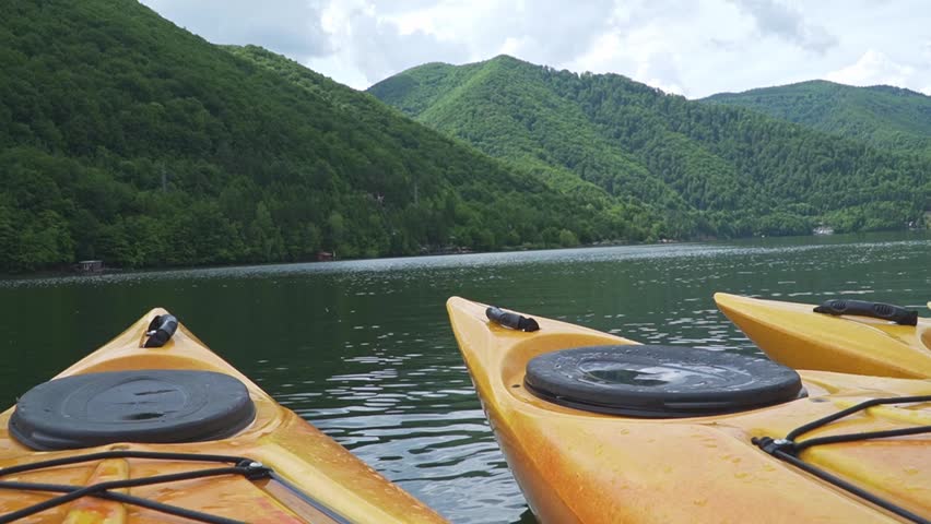 Yellow kayaks are positioned on a calm lake, framed by lush green hills under a cloudy sky.