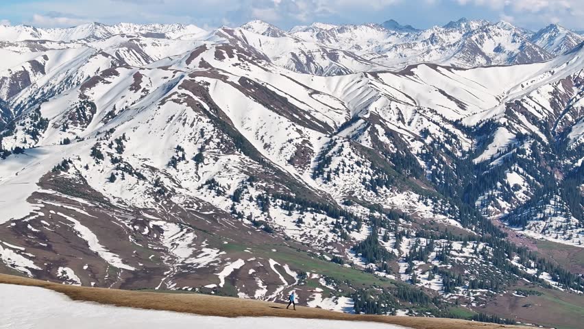Man is walking on mountain top, aerial epic high mountain background with snowy peaks, Kyrgyzstan.