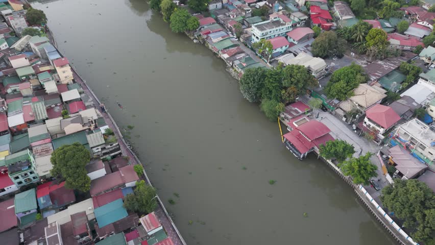 Drone footage moving forward above Pasig River, revealing riverside homes, urban neighborhoods, and tranquil waterways in Metro Manila, Philippines.