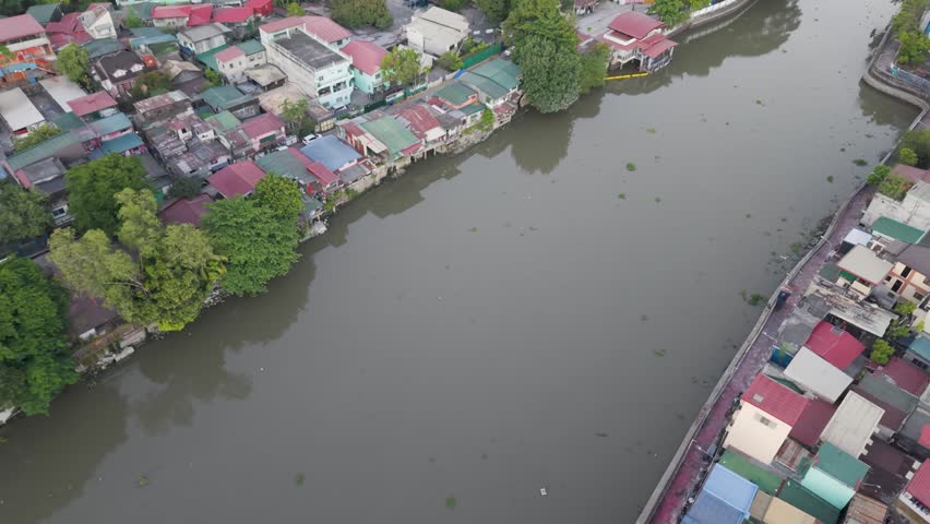 Drone footage moving forward above Pasig River with riverside homes, tree-lined banks, and urban neighborhoods in Metro Manila, Philippines.
