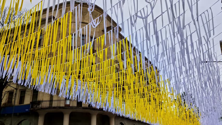 A low angle shot of bright yellow and white decorative ribbons hanging over a street in Tbilisi.
