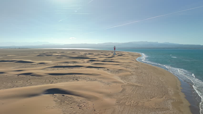 Fangar lighthouse surrounded by coastal dunes at Punta del Fangar in Ebro Delta Natural Park, Spain. Aerial drone view of iconic beacon, sandy landscape and Mediterranean shoreline.