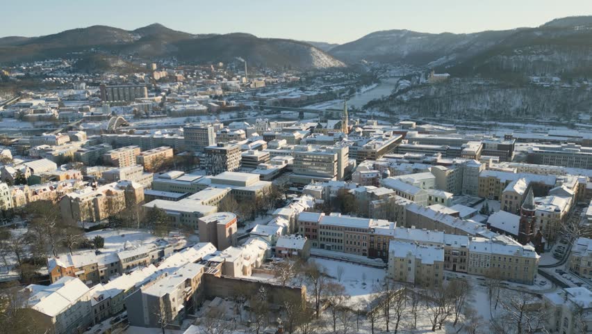 Aerial drone winter panorama of Ústí nad Labem city town under soft daylight, featuring snow-covered rooftops, the city center, and the winding Labe River winding through the surrounding hills
