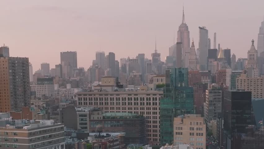 The skyline of New York City. Tall buildings fill the view as the sun sets, casting light over the streets. The city is alive with activity.