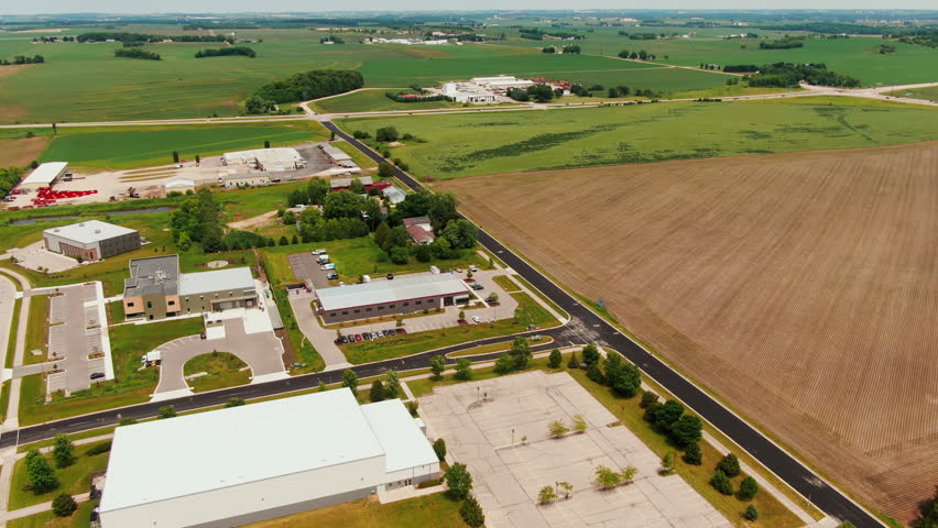 Backward aerial revealing shot of suburban area next to expansive farmland and industrial buildings in Waunakee, Wisconsin