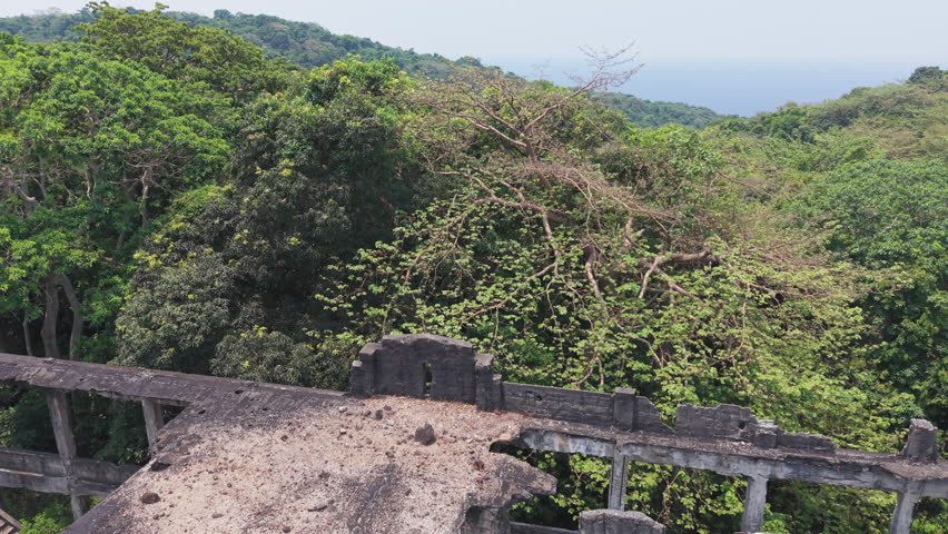 Close to wide drone shot of collapsed, vegetation-consumed WWII concrete ruins on Corregidor island, war dark history and heritage landmark.