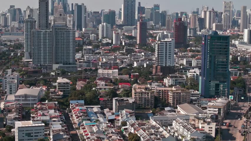 A wide view of Bangkok, Thailand, showing many buildings and homes in the city. The skyline features various structures under a clear sky during daylight.