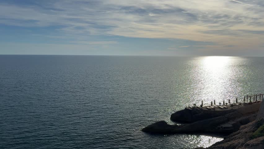 Sea glittering waters and rocky beach at dusk.