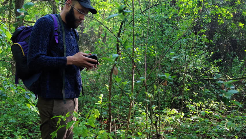 Bearded man wiping the lens of a trail camera with his sweater in a forest