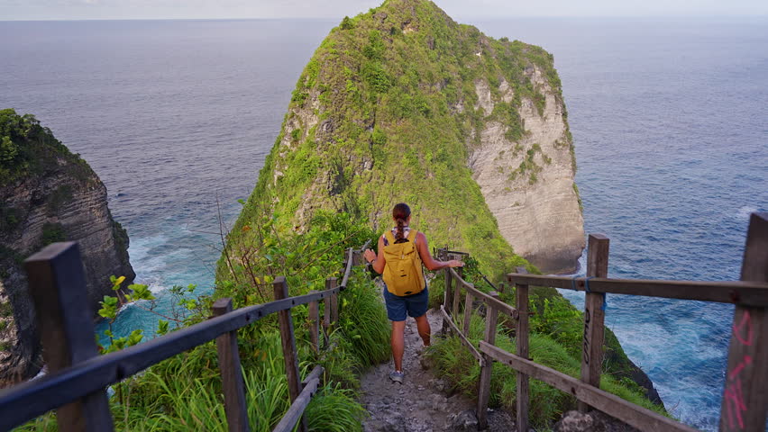 Female Traveler Descending Kelingking Beach Trail on Nusa Penida Island with Iconic Coastal Cliff View in Bali Indonesia.