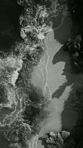 Sand shadows dance. Waves cast shadows over shorelines. Geometric silhouettes and textured surf patterns. Monochrome scene of shadows meeting water and textured sands, vertical video