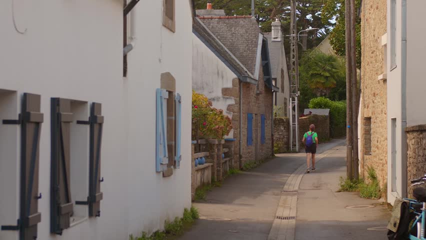 Traveler walking through a narrow traditional street lined with stone houses in Ile aux Moines, Brittany.
