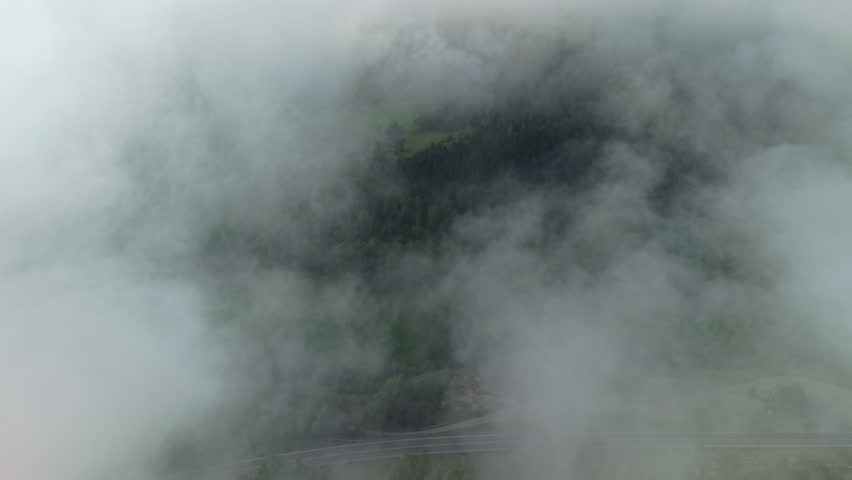 Drone flying through dense mountain clouds toward forested hills in Catalonia, Spain, aerial view of mist drifting over green woodland and countryside landscape