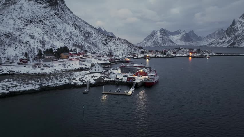 Aerial dusk view of a small snowy fishing village on a rocky fjord shore