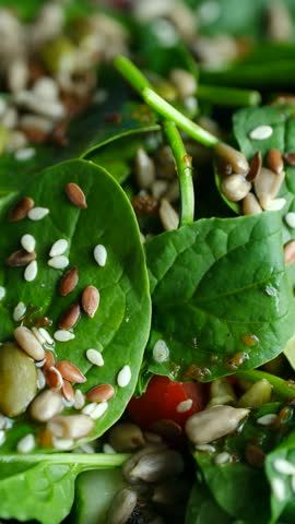 Delicious healthy green salad featuring fresh spinach leaves, cherry tomatoes, cucumbers, mix of nutritious seeds like sunflower, pumpkin, flax, and sesame, all tossed in light dressing. Vertical shot