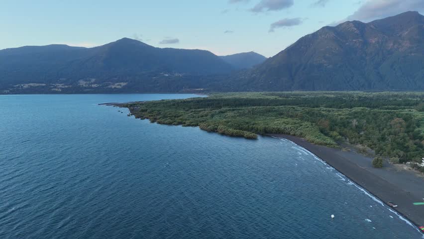Aerial over black sand beach, Rio Trancura delta, lush forest, Andes.