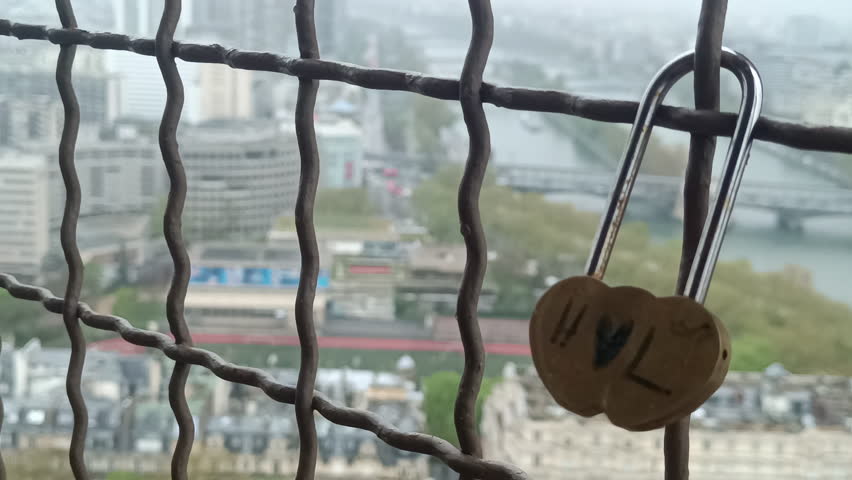 Heart-shaped love lock attached to a safety fence with a blurred view of Paris and The Seine River, eb01