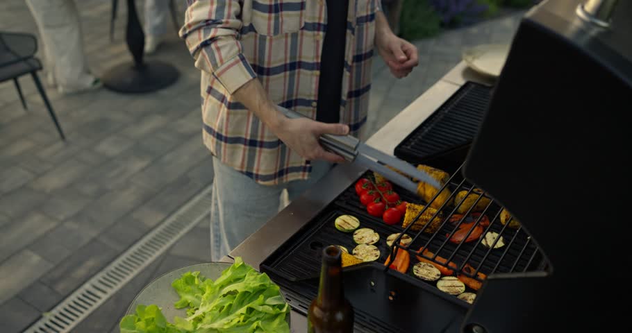 Man grilling assorted vegetables on an outdoor barbecue in a casual backyard patio setting
