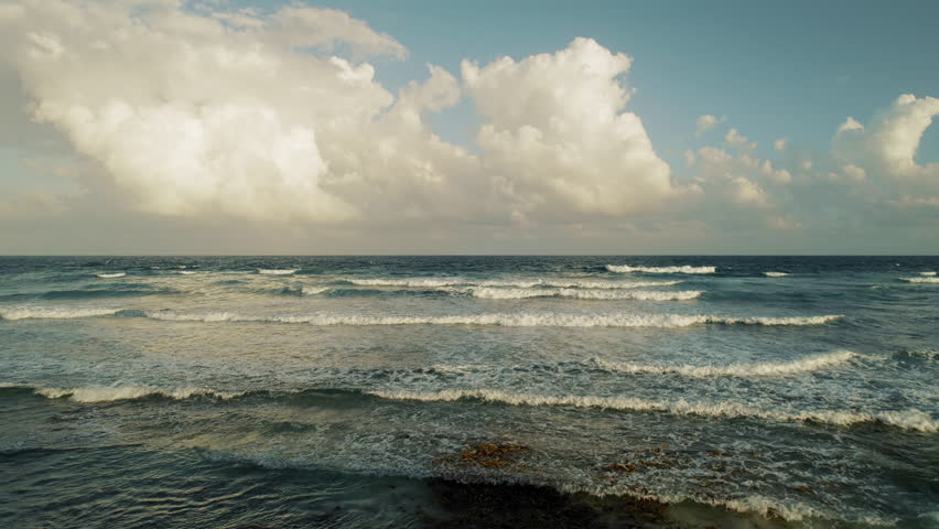 Sea waves ripple under golden sky on Yucatan shore as clouds tower in the distance