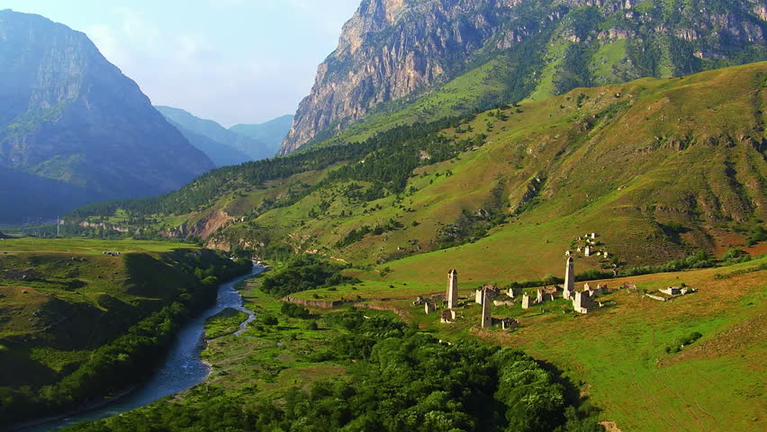 Ancient stone towers standing on a lush green hillside next to a winding river in a mountain gorge