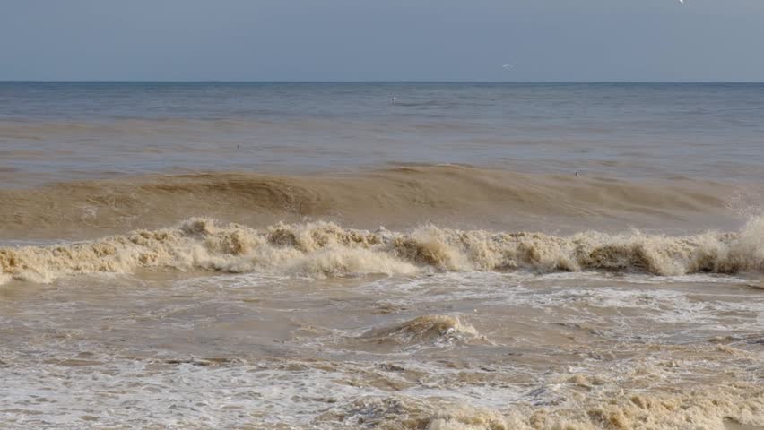 Large Muddy Waves Crashing onto Shore After Storm. Stormy Sea with Powerful Waves Hitting the Coast. Rough Brown Sea and Strong Coastal Wave Action.