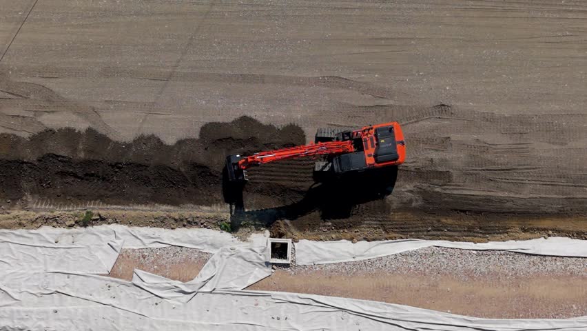 Aerial view of a railway infrastructure project in progress. A red bulldozer works on the ground preparation at the construction site.