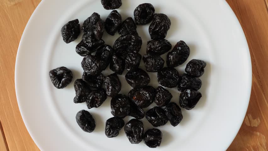 Top view of dried plums, also known as prunes, rotating on a white plate on a wooden table