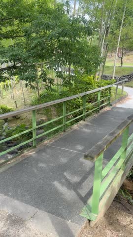 A pedestrian walkway with a green metal railing in a peaceful garden.