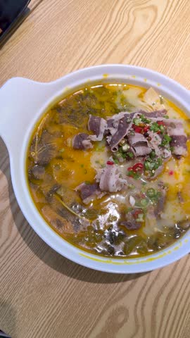 Top-down view of spicy beef soup in a white bowl on a wooden table.