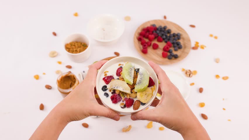 Overhead shot of hands arranging a nutritious breakfast bowl with kiwi, berries, and nuts.