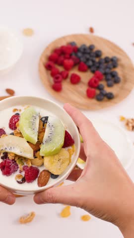 Person places a nutritious yogurt bowl topped with fresh fruit onto a bright table.