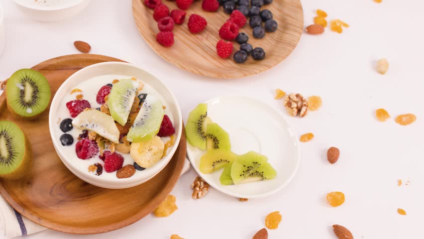 Top view of hands lifting a yogurt bowl topped with kiwi, berries, and nuts.