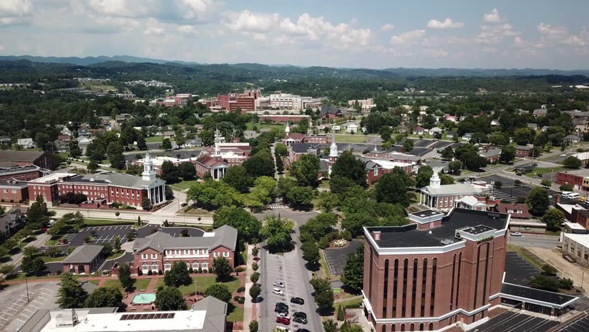 Drone perspective over a town with classic architecture, leafy trees, and distant hills. Aerial view of urban landscape.