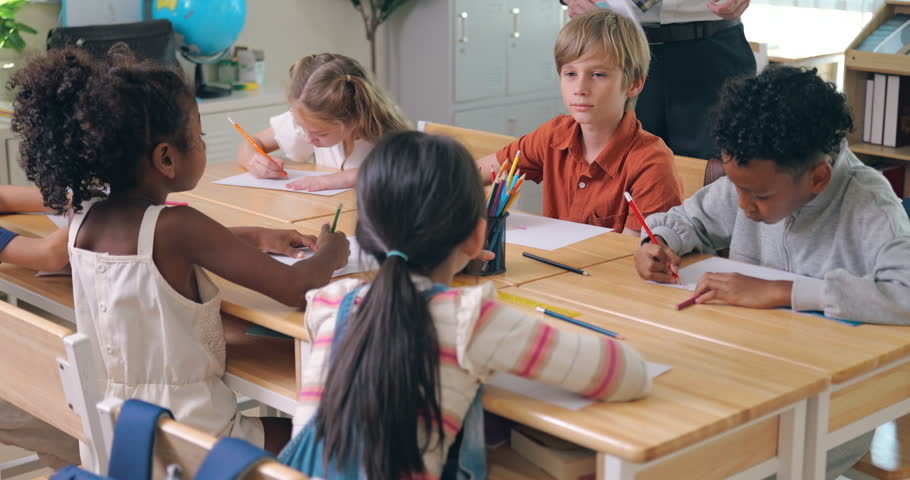 Multi-ethnic group of children sitting together at joined desks drawing and coloring.