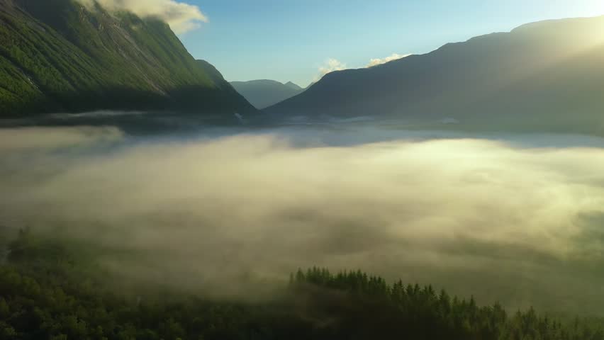Slow aerial shot of clouds rolling over forested mountain valley.