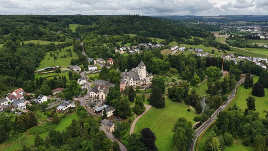 Expansive aerial view of the historic bourglinster castle surrounded by a charming village and lush green forests in the beautiful countryside of central luxembourg on an overcast day
