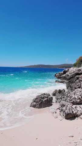Albania - Crystal clear turquoise sea water crasing against dark rocks and sandy beach on a beautiful sunny day.