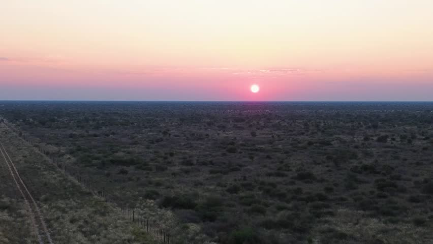 Blood red sunset camera rising up over the landscape of Khutse Game Reserve, Botswana. Landscapes combines most types of Kalahari habitat – rolling grasslands, river beds, fossil dunes, and grassed and bare pans. Aerial 4K Video.
