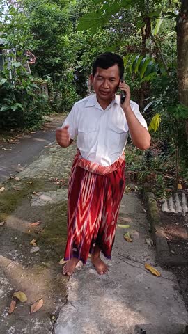 Happy Indonesian Man in Traditional Sarong Talking on Smartphone in Rural Village