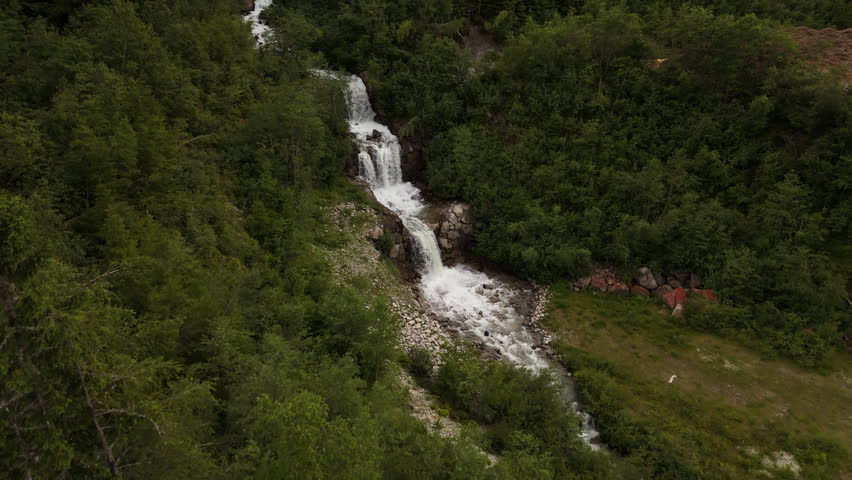 Aerial view tilting over a rushing alpine waterfall in Chamonix, summer in France