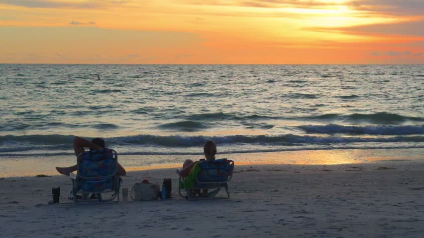 Silhouette of a couple in beach chairs watching the sunset at the beach in Florida