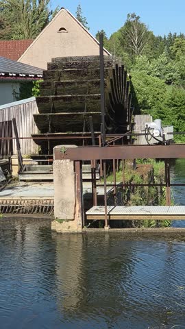 Close-up of an old wooden watermill wheel spinning on a river.