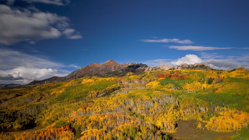 Aerial view of beautiful fall foliage on a mountainside with clouds casting shadows over the landscape.